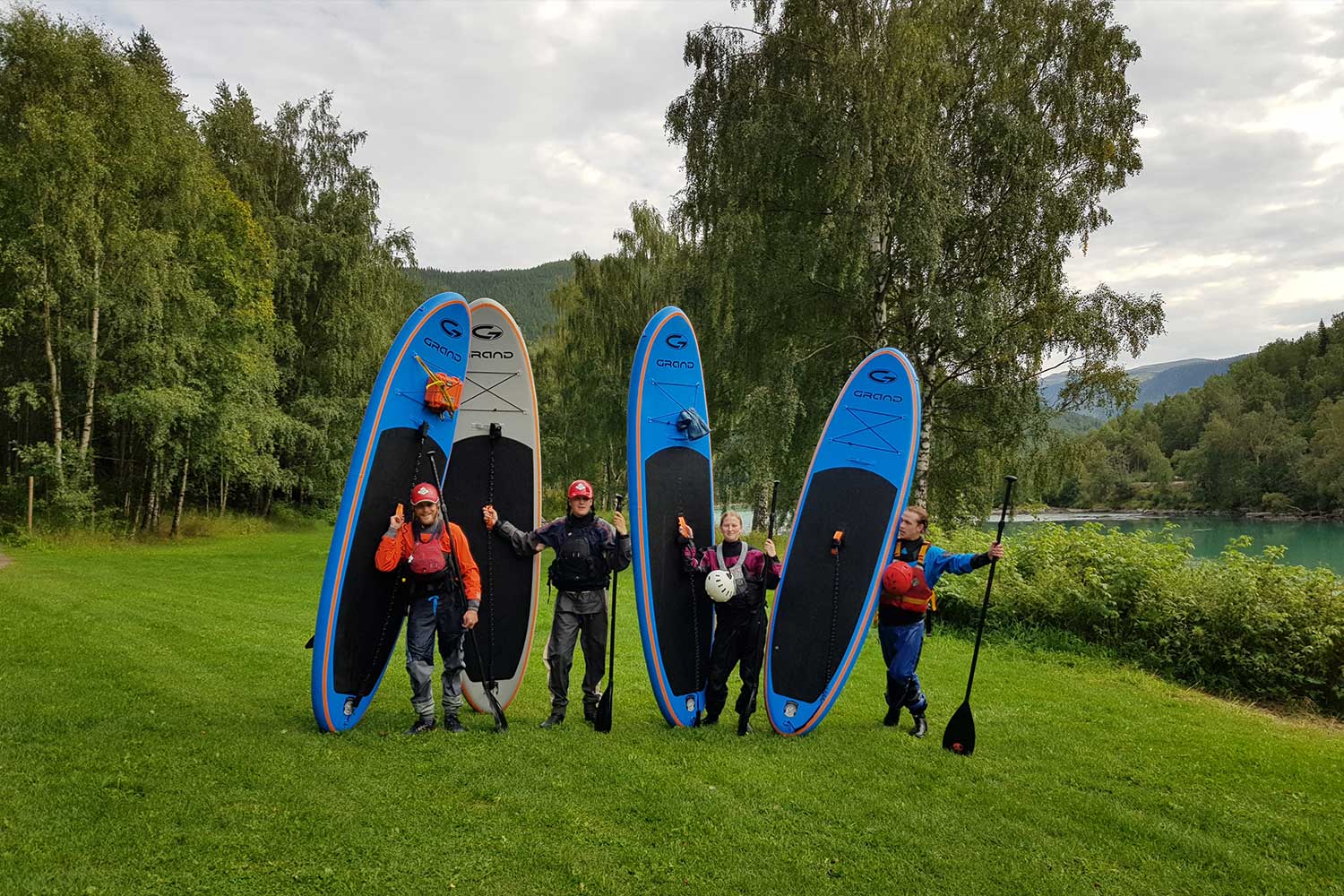 Fire personer stående på en gresslette med SUP brett