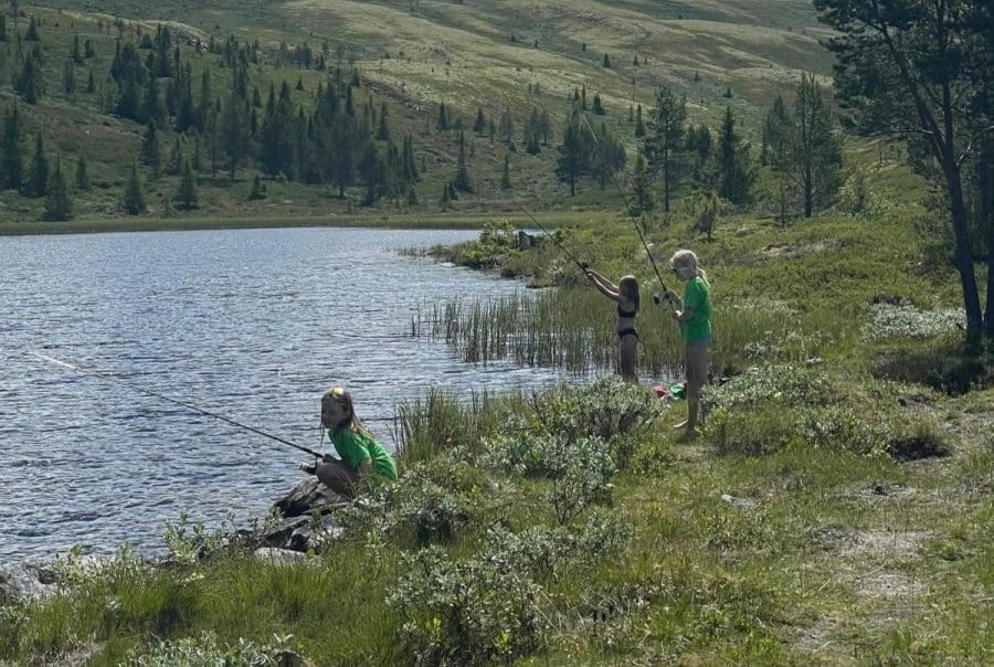 Barn fisker ved en idyllisk innsjø under en villmarksdag på sommerleir i Sjoa.