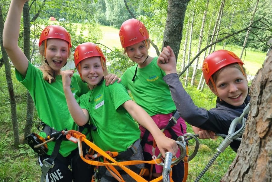 Barn smiler mens de klatrer i Sjoa klatrepark under sommerleir.